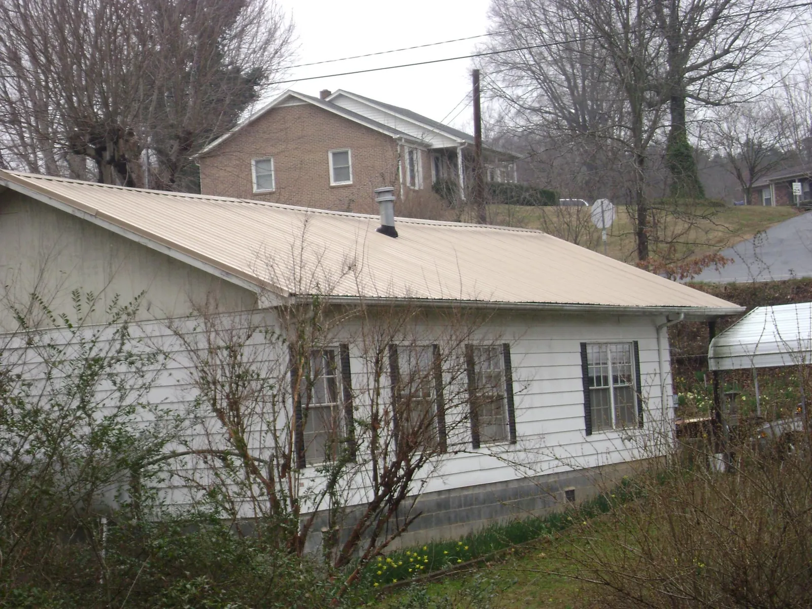 Tan metal roof on a white sided house set into a hillside — Commercial Roofing by Roofing Brothers in Abilene